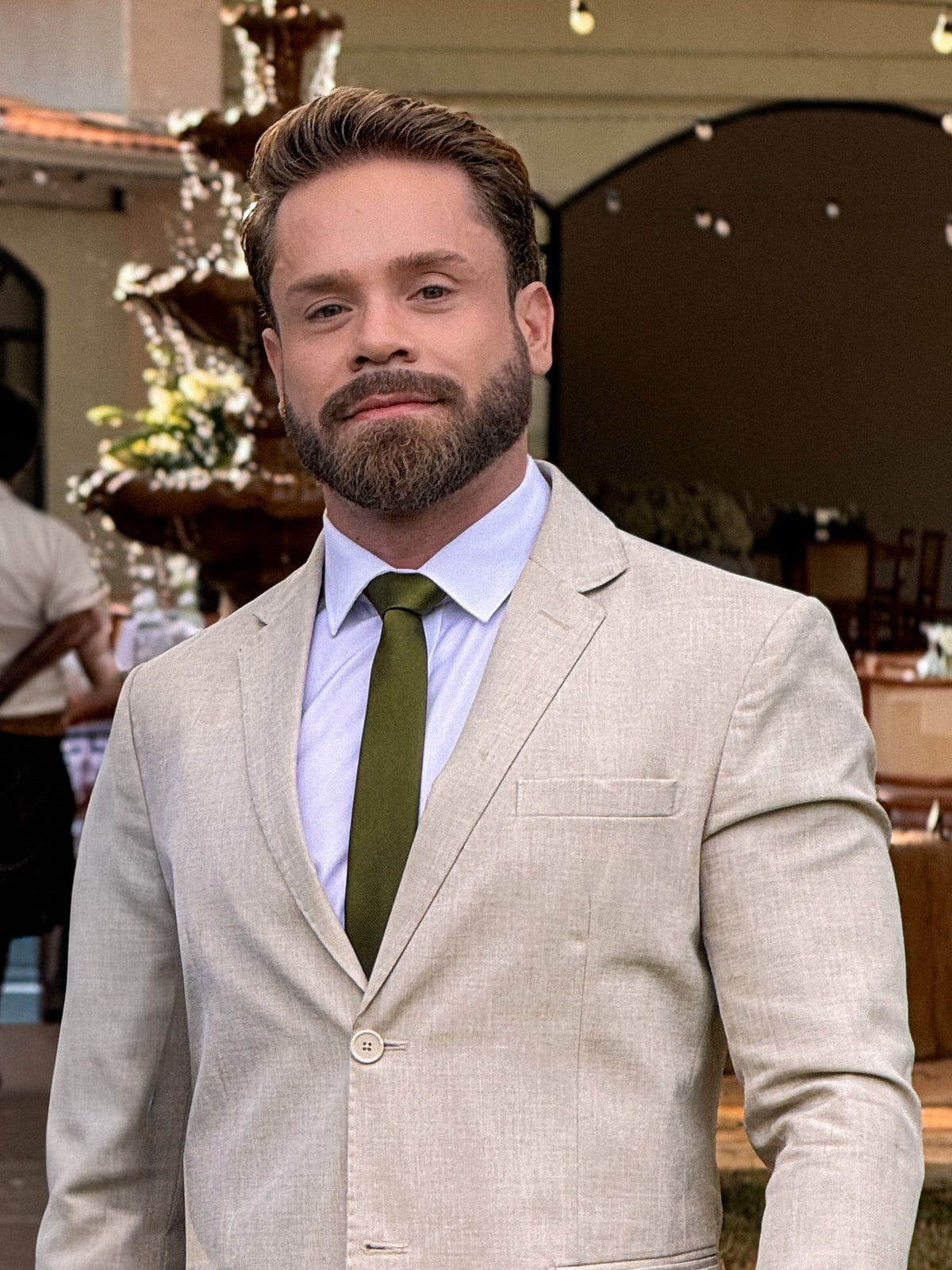 Marcos Malfer, fundador da Vettix AI. Homem de barba cheia, terno claro de linho, camisa azul-clara e gravata verde-oliva, olhando para a câmera.